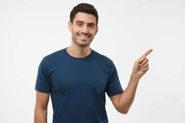 Hombre joven vestido casual en camiseta azul apuntando a la derecha con el dedo aislado sobre fondo gris — Foto de Stock