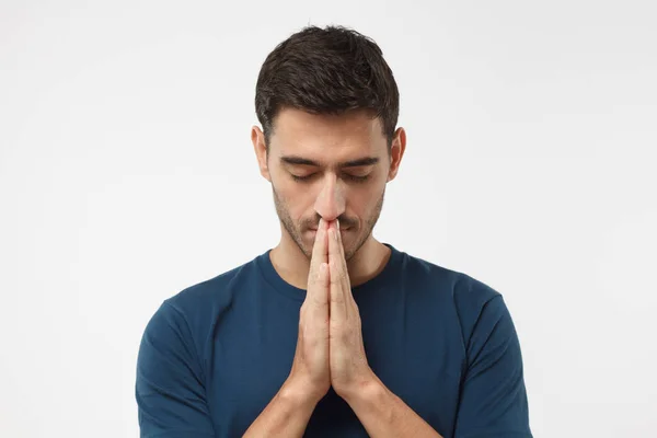 Close-up van jonge man geïsoleerd op grijze achtergrond op zoek gestresst, handen samen te stellen, alsof hij aan het bidden is met gesloten ogen te overwinnen depressie en vinden van de oplossing voor probleem — Stockfoto