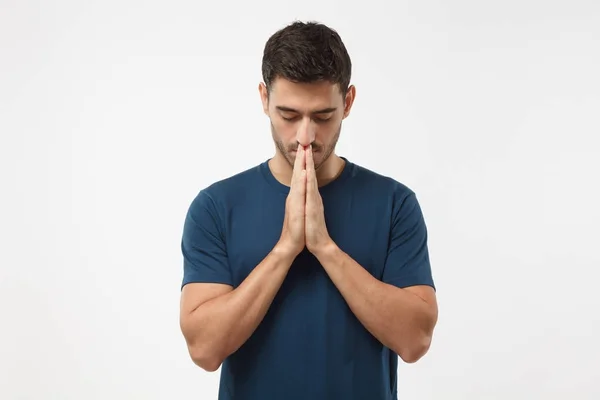 Picture of young guy dressed casually isolated on grey background, having put hands together in prayer or meditation, looking relaxed and calm, dreaming and waiting for all best — Stock Photo, Image