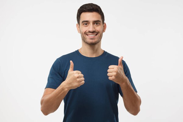 Closeup of young optimistic man isolated on grey background showing thumps up with positive emotions of content and happiness. Concept of satisfaction with quality and recommendation