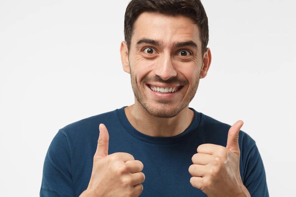 Close up shot of motivated excited young male making a thumbs up gesture of approval and success with smile