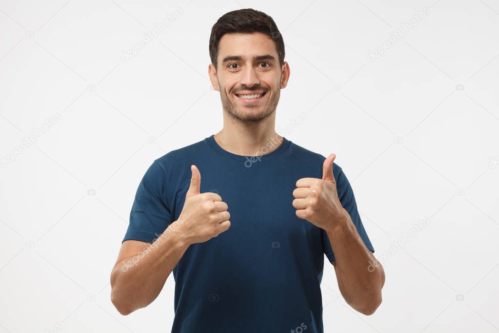 Closeup of young optimistic man isolated on grey background showing thumps up with positive emotions of content and happiness. Concept of satisfaction with quality and recommendation