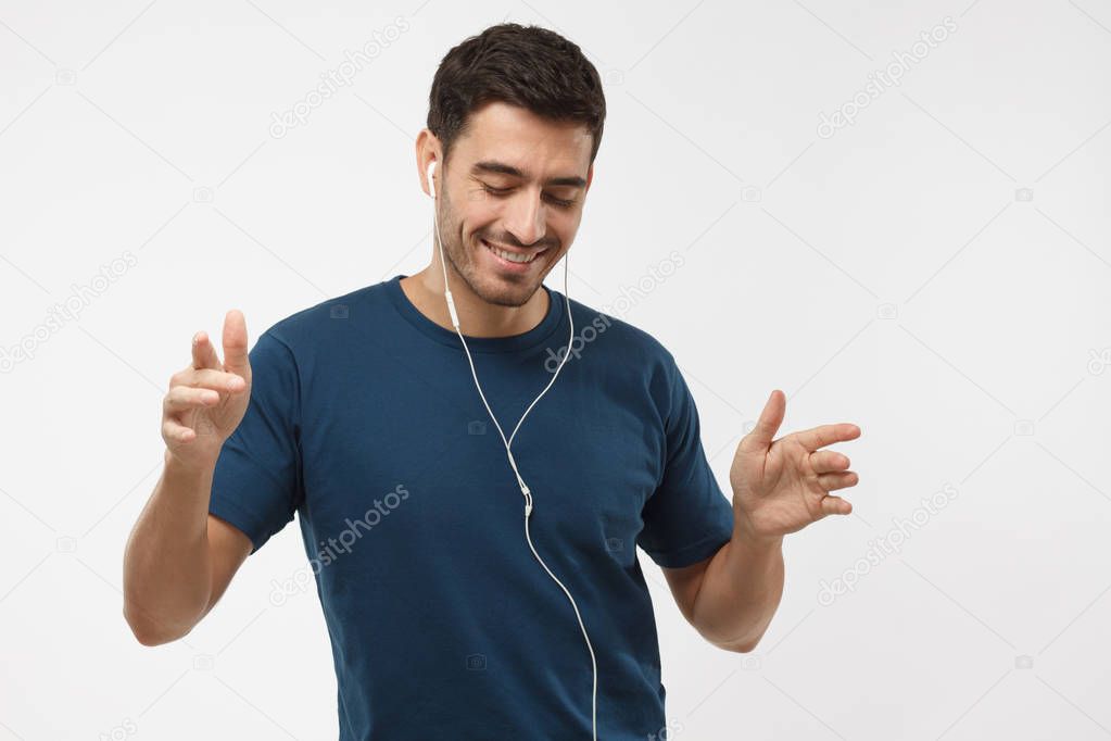 Young happy man smiling, listening music via headphones, dancing with closed eyes isolated on gray background. My favourite song