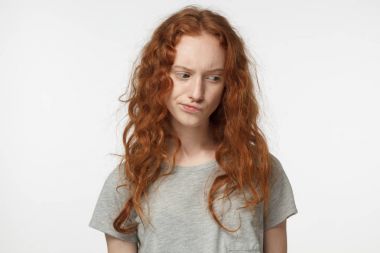 Genç güzel kızıl saçlı Avrupa erkek ile bağsız kıl, şüphe ve alaycı yüzünde memnuniyetsizlik ifadesi ile bakıyordu gri T-shirt giyen beyaz arka plan üzerinde izole kapalı portresi