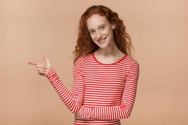 Çizgili tişört bej renkli arka plan üzerinde izole parmağı ile sol işaret içinde çekici genç Kızıl saçlı erkek