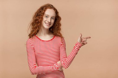 Çizgili tişört şu şeftali arka plan üzerinde izole parmak ile işaret içinde çok kıvırcık saçlı kız