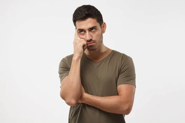 Thoughtful young man in olive t-shirt, gesturing with hand, solving relationship or health problem. Doubt concept. — Stock Photo, Image