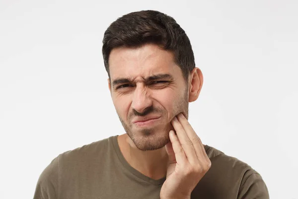 Indoor headshot van jonge mannelijke gevoel pijn, zijn wang met de hand te houden, lijdt aan slechte kiespijn, op zoek naar camera met pijnlijke expressie. Tand pijn concept. — Stockfoto