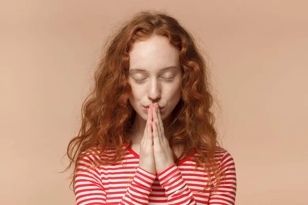 Primo piano di attraente giovane rossa donna a righe t-shirt mettendo insieme le mani come se stesse pregando con gli occhi chiusi — Foto Stock