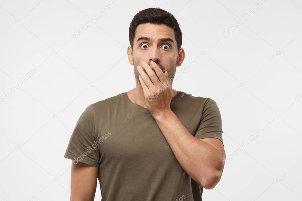 Astonished bug-eyed student covering his mouth with one hand, looking shocked. Surprised, embarrassed and confused young male showing omg emotion