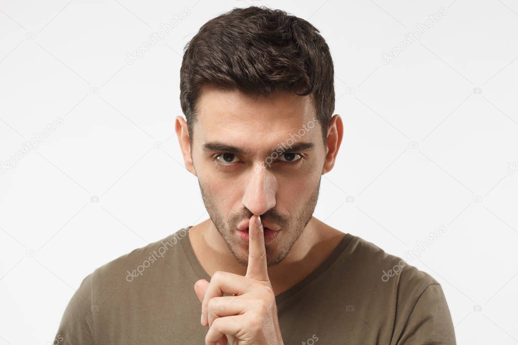 Close up shot of handsome male with shhh gesture, asking for silence or to be quiet, isolated on gray background