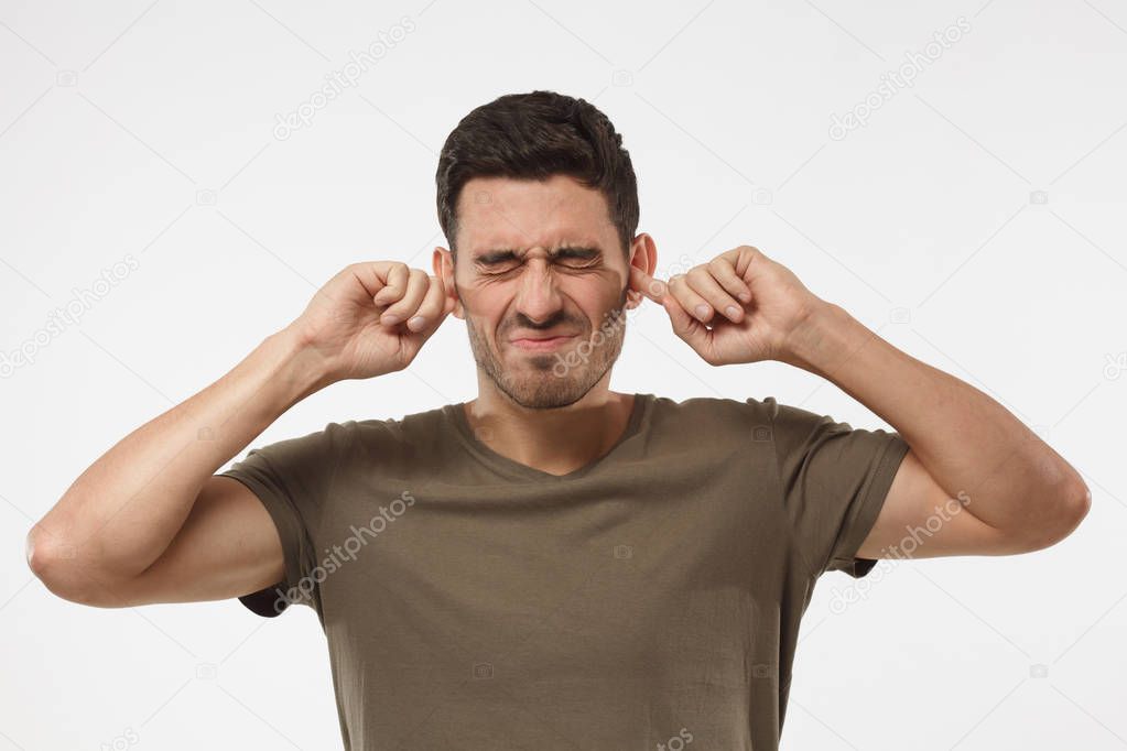 Stressed frustrated young man plugging his ears with fingers and keeping eyes closed while having headache, can't stand terrible noise around from neighbours