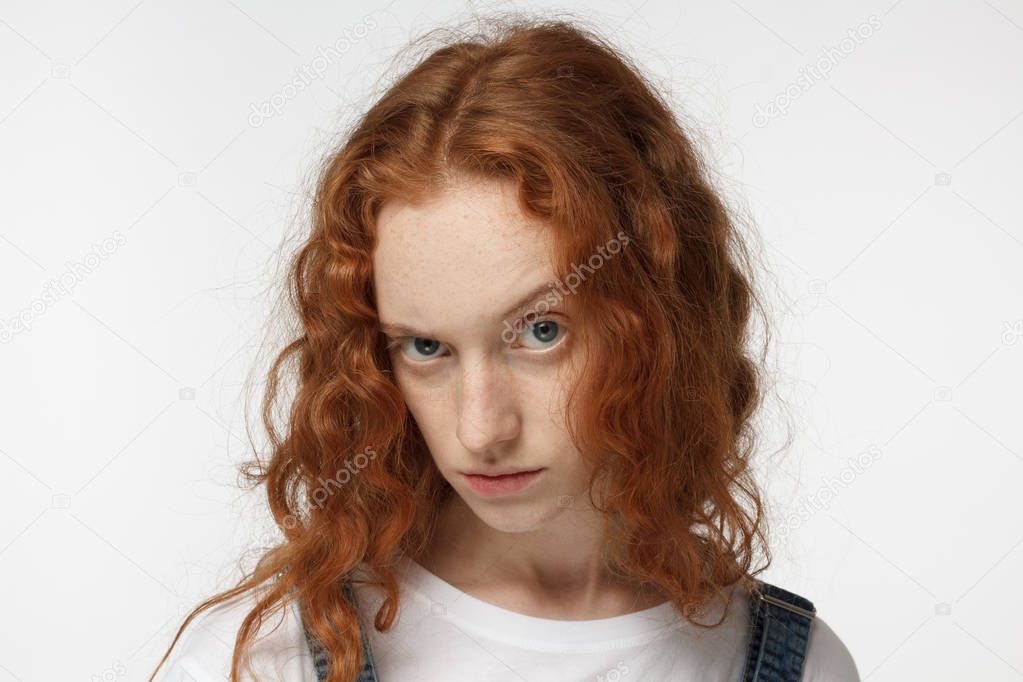 Closeup photo of young attractive redhead European female isolated on white background with curly hair looking suspiciously at interlocutor having doubt about presented ideas and questioning them