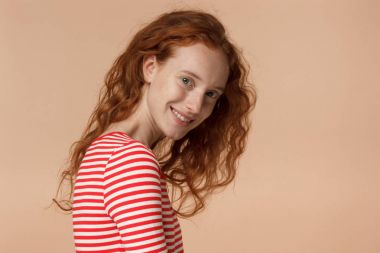 Portre portre genç redhead omuz kamera, açık Avrupa kadın resim üzerinde izole şeftali arka plan aşağı düşen, rahat seyir gevşek kıvırcık saçları ile mutlu bir şekilde gülümseyerek