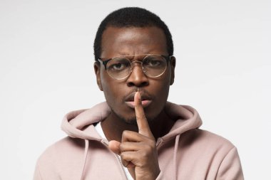 Sessizlik için veya sessiz olmak isteyen yakışıklı siyah erkek shhh hareketi ile atış izole üzerinde gri arka kapatmak