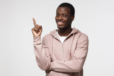 Pembe kapşonlu gri arka plan üzerinde izole parmağıyla yukarıyı çekici genç siyah adam