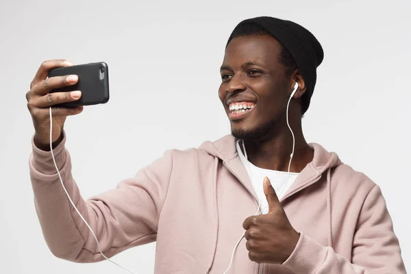 Foto van de knappe zwarte man geïsoleerd op een grijze achtergrond, strekken van de arm met smartphone om selfie foto te delen in sociale netwerken — Stockfoto