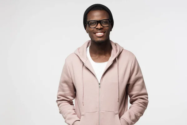 Portret van lachende knappe Afro-Amerikaanse jongen in roze hoodie staande geïsoleerd op een grijze achtergrond — Stockfoto