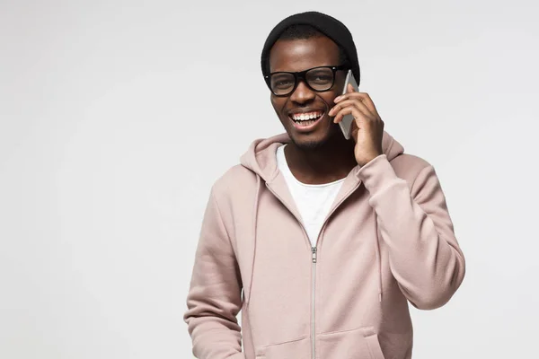 Nahaufnahme Porträt eines jungen schwarzen Mannes in rosa Kapuzenpulli, der seinem Kumpel auf dem Handy zuhört, entspannt und fürsorglich mit einem Lächeln aussieht — Stockfoto