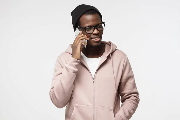 Close-up van de indoor van jonge African American man geïsoleerd op een witte achtergrond, het dragen van casual kleding van de hipster en grote glazen, praten over de telefoon met tevreden vriendelijke glimlach, horen aangenaam nieuws — Stockfoto