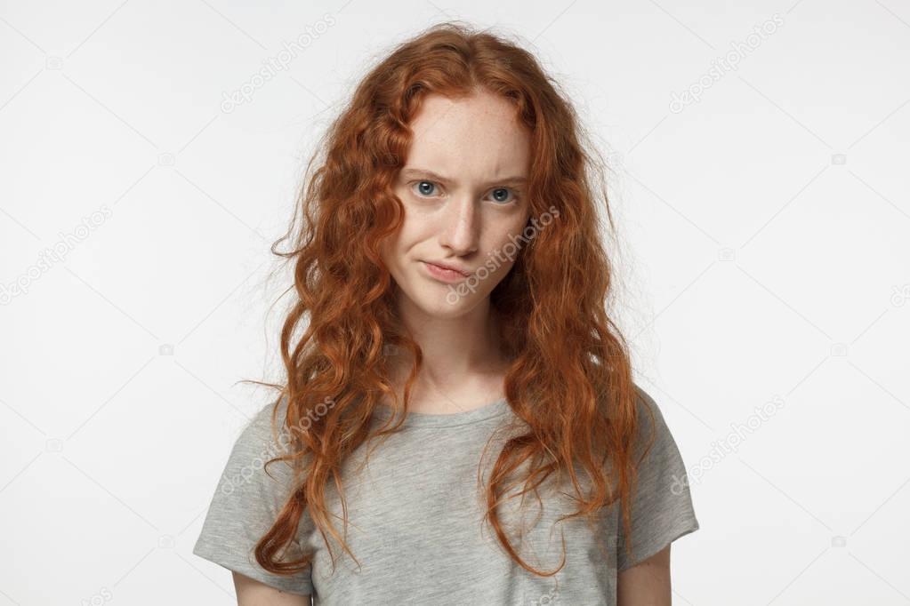 Horizontal closeup photo of teenage redhead European girl isolated on white background frowning and curling her lips showing deep mistrust and doubt as if disagreeing with what she hears or sees