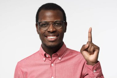 Pembe gömlek ve gri arka plan üzerinde izole parmağıyla yukarıyı gözlük çekici genç bir siyah adam