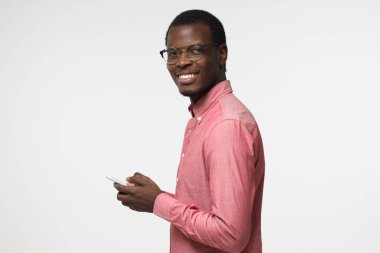 Genç çekici Afrika erkek görünümlü ve manifatura süre neşeli ifade ile kamera cep telefonu, gri arka plan üzerinde izole kullanarak arkadaşları, gülümseyen