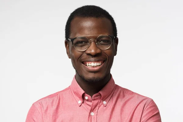 Close-up shot van jonge Afrikaanse man in ronde bril afgebeeld geïsoleerd op witte achtergrond dragen casual kleding, tonen toothy open smile, op zoek naar positieve en vol vertrouwen, tevreden leven — Stockfoto