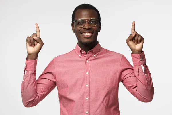 Knappe zwarte man in roze t-shirt omhoog met twee vingers geïsoleerd op een grijze achtergrond — Stockfoto