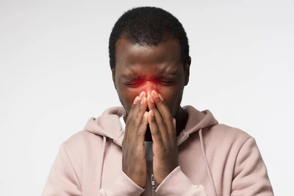 Lichaamstaal. Zieke Afrikaanse jongeman in roze hoodie over gezicht met handen; niezen; geïsoleerd op een grijze achtergrond — Stockfoto