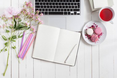 Kadınsı düz çalışma alanı ile laptop, fincan çay, macarons ve çiçekler, planlayıcısı ve kalemi Beyaz ahşap masa üzerinde yatıyordu. Üstten Görünüm kadar sahte.