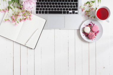 Kadınsı düz çalışma alanı laptop, fincan çay, macarons ve beyaz tahta masaya çiçek ile yatıyordu. Üstten Görünüm kadar sahte.