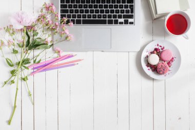 Kadınsı düz çalışma alanı laptop, fincan çay, macarons ve beyaz tahta masaya çiçek ile yatıyordu. Üstten Görünüm kadar sahte.