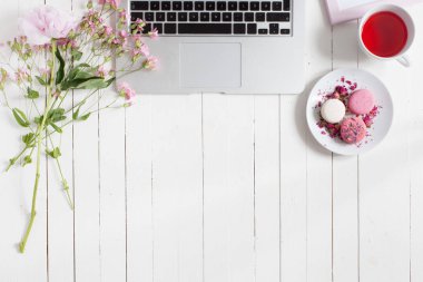 Kadınsı düz çalışma alanı laptop, fincan çay, macarons ve beyaz tahta masaya çiçek ile yatıyordu. Üstten Görünüm kadar sahte.