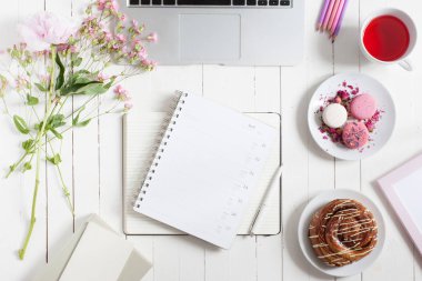 Kadınsı düz çalışma alanı laptop, fincan çay, planlayıcısı, macarons ve beyaz tahta masaya çiçek ile yatıyordu. Üstten Görünüm kadar sahte.