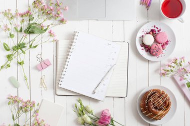 Kadınsı düz çalışma alanı laptop, fincan çay, planlayıcısı, macarons ve beyaz tahta masaya çiçek ile yatıyordu. Üstten Görünüm kadar sahte.