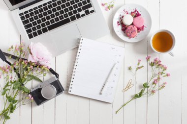 Kadınsı düz çalışma alanı laptop, fincan çay, planlayıcısı, macarons ile yatıyordu. Retro kamera ve beyaz tahta masaya çiçek. Üstten Görünüm kadar sahte.