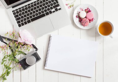 Boş karalama defteri. Kadınsı düz çalışma alanı laptop, fincan çay, macarons ve beyaz tahta masaya çiçek ile yatıyordu. Üstten Görünüm kadar sahte.