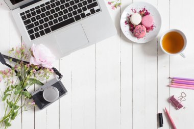 Kadınsı düz çalışma alanı laptop, fincan çay, retro kamera, macarons ve beyaz tahta masaya çiçek ile yatıyordu. Üstten Görünüm kadar sahte. Metniniz için boş alanı. 