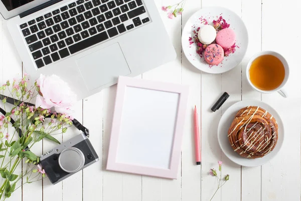 Pink frame with marker. Feminine flat lay workspace with laptop, cup of tea, planner, macarons and flowers on white wooden table. Top view mock up.