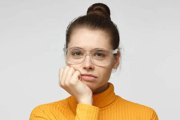 Close up retrato de jovem fêmea entediada em óculos com cabeça no queixo isolado no fundo cinza — Fotografia de Stock