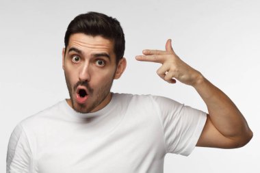 Genç adam intihar parmak silah hareketi ile kendini parmak tabanca işareti, gri arka plan üzerinde izole yapma çekim