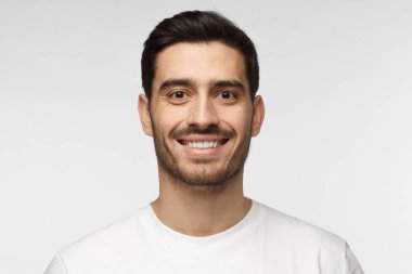 Yakışıklı adam beyaz t-shirt gri arka plan üzerinde izole gülümseyen portresi kapatın