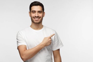 Beyaz t-shirt şu gri arka plan üzerinde izole parmağıyla işaret içinde çekici genç adam