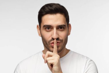 Zor yakışıklı ile vurdu kadar sessiz sessizlik için veya sessiz olmak isteyen bir jest, gri arka plan üzerinde izole kapatmak