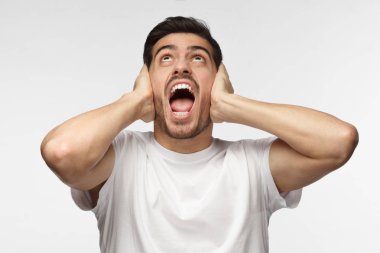 Genç yakışıklı adam bağırmak gürültülü komşular, gürültü, kulakları her iki el ile kapatma tarafından vurguladı önlemek dinleme mücadele