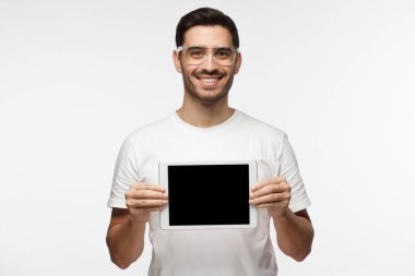 Tablet tutarak ve ürün veya hizmet danışmanlık sanki boş ekran mutlu gülümseme ile gösterilen rahat kıyafetler içinde duran gri arka plan üzerinde izole olumlu adam stüdyo resmi