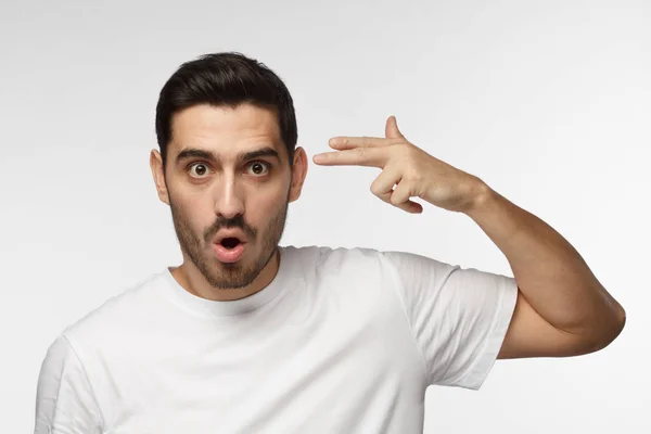 Attractive man having problems, makes suicide gesture, pretends shooting himself, wants to avoid all troubles, isolated on grey background — Stock Photo, Image