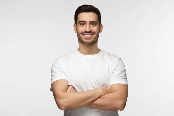 Retrato de hombre guapo sonriente en camiseta blanca de pie con brazos cruzados aislados sobre fondo gris — Foto de Stock