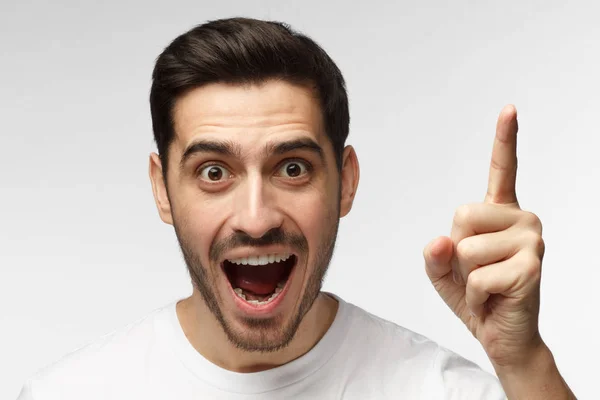 Retrato de cerca del joven guapo hombre sonriente con camiseta blanca, señalando con el dedo en el signo de eureka, teniendo una gran idea innovadora, comprensión o solución que acaba de obtener — Foto de Stock